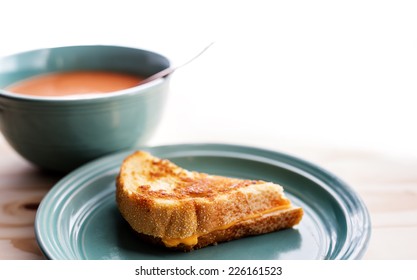 Half A Grilled Cheese Sandwich With A Bowl Of Tomato Soup. 