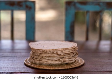 A half kilogram of freshly made tasty corn / maize Mexican tortillas, a staple of Mexican cuisine. On an outside wooden table, with rustic vintage green painted chairs in the background. - Powered by Shutterstock