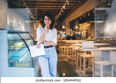 Half length of cheerful Caucaisan entrepreneur feeling success in franchise coffee shop standing in doorway and smiling at camera, happy self employed woman working in local cafeteria industry - Powered by Shutterstock