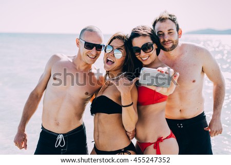 Half length of group of young multiethnic friends women and men at the beach in summertime taking selfie in the water having fun smiling - friendship, smiling, happiness, social network concept