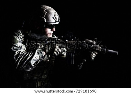 Half length low angle studio shot of special forces soldier in field uniforms with weapons, portrait on black background. Protective goggles glasses are on