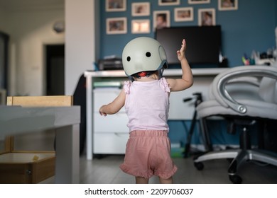 Half Length Of One Girl Small Caucasian Toddler Baby Wear Protective Helmet On Head While Standing Or Walking At Home In Room Growing Up Learning New Skills Early Development Concept Back View