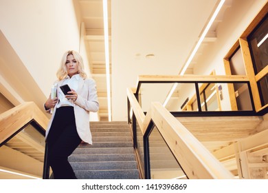 Half Length Portrait Of Attractive Caucasian Female Economist Looking At Camera On Way For Business Meeting, Executive Manager Using Digital Phone For Communicate On Stairs In Modern Workshop