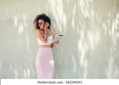 Half Length Portrait Of Attractive Curly Hair Female Standing With Touch Pad Against Copy Space Area Holding Touch Pad. Well Dressed Woman Using Networking Connection To Internet On Her Digital Tablet