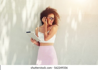 Half length portrait of attractive curly hair female standing with touch pad against copy space area holding touch pad. Well dressed woman using networking connection to internet on her digital tablet