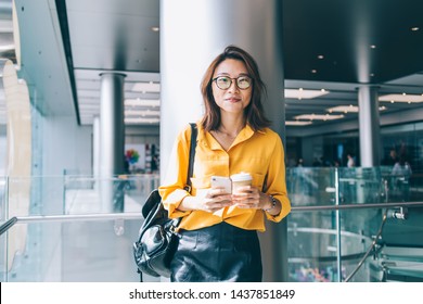 Half length portrait of attractive female blogger in optical spectacles for provide eyes protection smiling at camera during coffee break for networking with cellphone gadget, millennial person