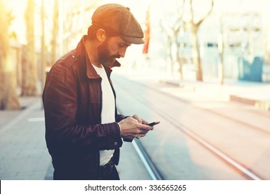 Half Length Portrait Of Bearded Male With Retro Style Using Cell Telephone While Standing In Urban Setting, Man Dressed In Stylish Clothes Chatting On Smart Phone During Walking In Cool Spring Day 