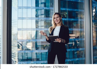 Half Length Portrait Of Beautiful Caucasian Female Manager In Elegant Formal Suit Standing Near Panoramic Window With Digital Tablet, Smiling Prosperous Business Woman Satisfied With Successful Career