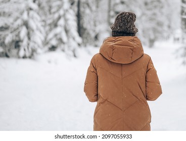 Half length portrait of brunette girl wearing brown long jacket and hat. standing pose in snow forest
