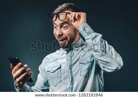 Half length portrait of casually dressed bearded man looking surprized after winning online lottery. Lucky winner making bets online using gambling application on his mobile phone.