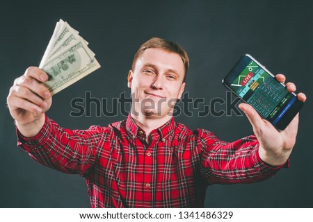 Half length portrait of casually dressed business man holding ward of cash celebrating his success after making bets online in mobile gambling application. 