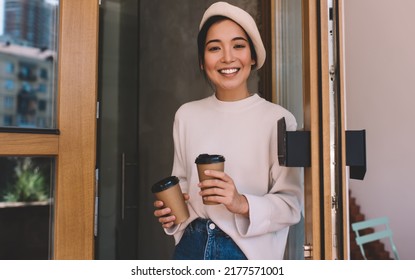 Half Length Portrait Of Cheerful Asian Hipster Girl With Two Disposable Cups Of Caffeine Beverage Smiling At Camera, Happy Female Customer 20s Holding Coffee To Go As Takeaway Cafeteria Order