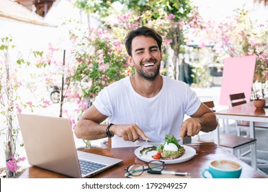 Half Length Portrait Of Cheerful Caucasian Male Eating Healthy Meal Satisfied With Brunch Laughing In Good Mood, Positive Funny Hipster Guy Keeping Healthy Lifestyle Enjoying Vegan Food In Cafe