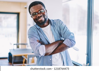 Half length portrait of cheerful dark skinned male entrepreneur in casual wear standing with crossed arms satisfied with completed job,african american funny guy laughing and looking at camera