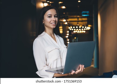 Half length portrait of successful female secretary with laptop computer in hands smiling at camera during workflow in office interior, happy Caucasian proud CEO 20 years old posing with netbook