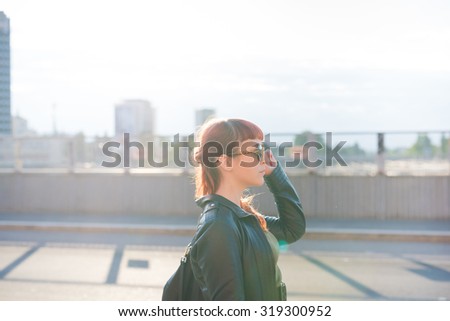 half length profile of a young handsome caucasian redhead woman walking in the city, overlooking left, pensive - seriousness concept - backlight - wearing a leather jacket 