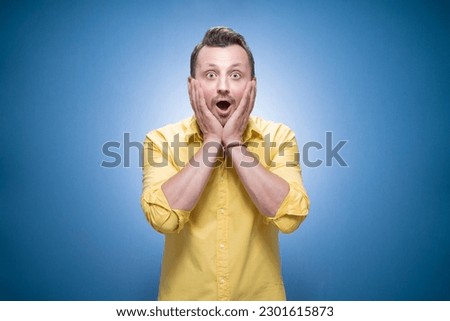 Half length thrilled young man over blue background, dresses in yellow shirt. Surprised bearded guy. Unbelievable concept. Amazement. Studio shot