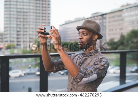 Half length of young beautiful afro black man outdoor in the city holding a smart phone taking picture - technology, social network, travel concept