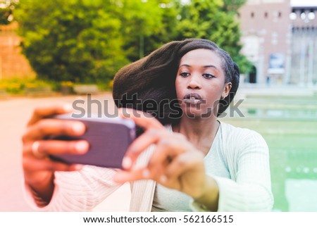Half length of young beautiful afro black woman outdoor in the city holding a smart phone taking selfie - technology, vanity, social network concept