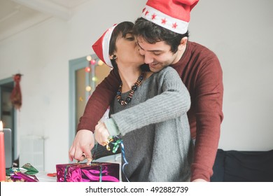 Half length of young handsome caucasian man and woman couple wrapping christmas present with wrapping paper and ribbon he is hugging her from back, smiling - christmas, couple, holiday concept - Powered by Shutterstock