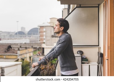 Half length of young handsome man standing on a balcony outdoor, overlooking, serious - pensive, thoughtful, thinking future concept