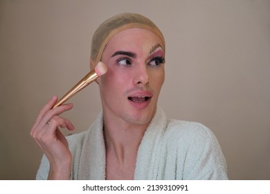 Half man half woman make up person. Drag queen person with a make-up brush wearing bathrobe. Male makeup artist.