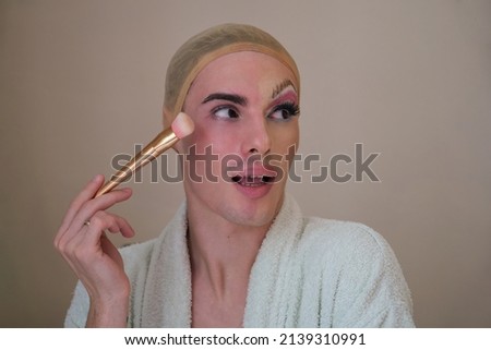 Half man half woman make up person. Drag queen person with a make-up brush wearing bathrobe. Male makeup artist.