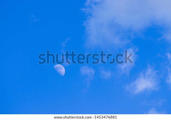Half moon in the\
daytime sky with clouds.