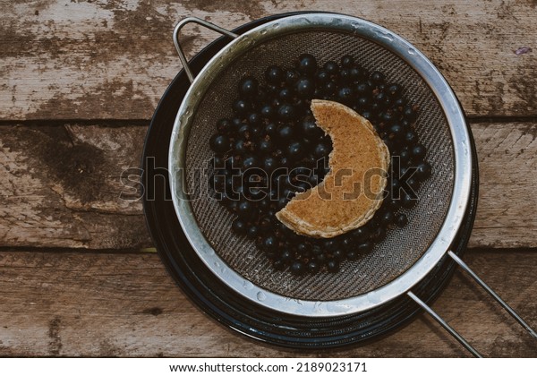 Half moon oat pancake.\
A metal sieve with\
currant berries and a pancake.\
