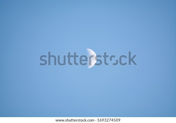 Half moon on blue sky background. Night sky\
wallpaper over the city. Cityscape glowing moon phase. Mysterious\
astronomy night light. Science cosmos midnight half circular\
luminescent moon.