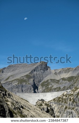 A half moon rising over the Cabane de Vieux Emosson alpine refuge mountain station next to the hydroelectric power station dam wall of the Vieux Emosson in Switzerland