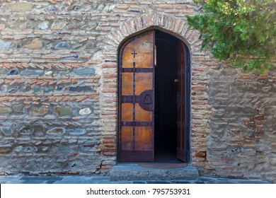 A half open wooden door of the church against the backdrop of a stone wall. Wooden doors of the church.