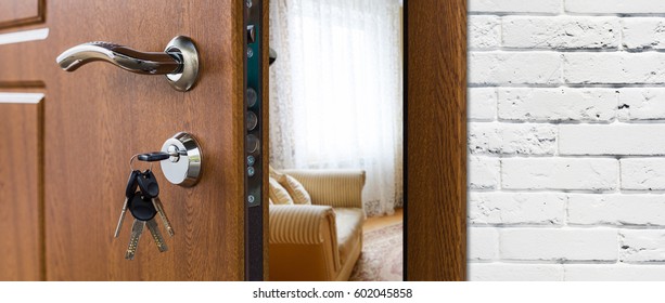 Half opened door handle closeup, entrance to a living room. Welcome, privacy concept. Door lock with keys, white brick wall, modern interior design.