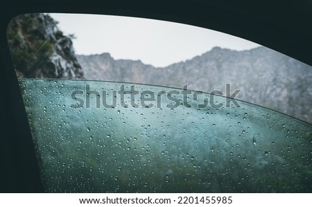 Half opened front car door misted window covered with a cold rain drops with a rocky mountains range and heavy stormy clouds.   商業照片 © 
