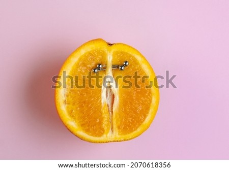 Half an orange with  vertical barbell piercing on a pink background.
