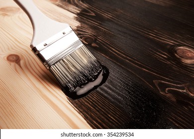 Half painted wooden surface. Black color. Varnishing natural wood with paint brush.