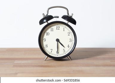 It is half past four. The time is 4:30 am or pm. Four thirty o'clock. Retro clock isolated on a wooden table. White background. Copy space.