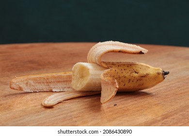 Half peeled ripe banana on the wooden table. bitten banana. Speckled banana peel