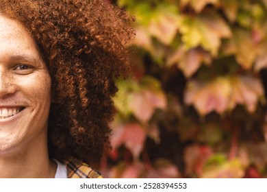 Half portrait of happy biracial man with red curly hair smiling in autumn garden, copy space. Free time, lifestyle, nature and wellbeing, unaltered. - Powered by Shutterstock