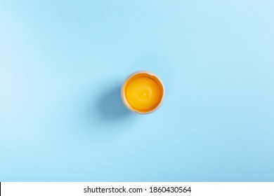 Half raw chicken egg with yolk on light blue background. Flat lay, copy space, top view.
