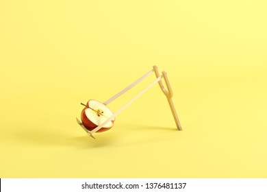 Half of red apple in a slingshot on yellow background. Minimal fruit idea concept.