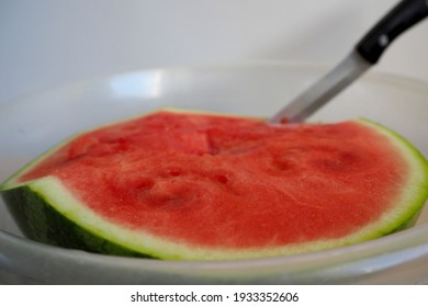 Half A Red Juicy Watermelon With A Knife In A Clear Plastic Bowl Side View