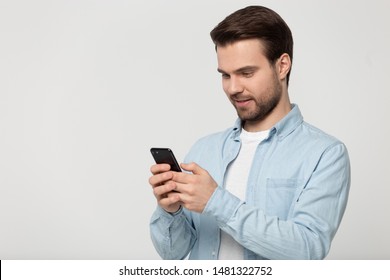 Half Side Head Shot Young Happy Man Standing Aside Empty Blank Copy Space For Advertising Text, Product Or Service Promo, Holding Phone, Looking At Screen, Isolated On Grey White Studio Background.