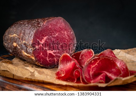 Half a smoked bresaola and cut pieces on a chopping Board. Italian Antipasti, rustic style