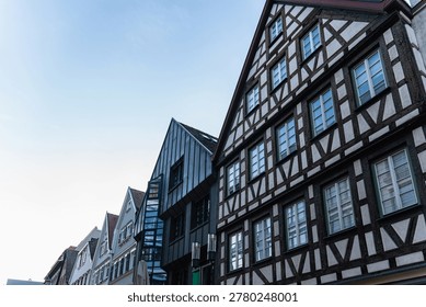 Half timbered building facade with windows beside neighboring structures along a narrow street under clear sky.