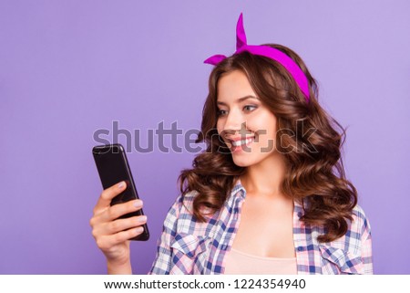Half turn portrait of pretty charming cheerful carefree careless lady with her hairstyle she isolated on bright purple background hold gadget in hand look on screen receive send sms