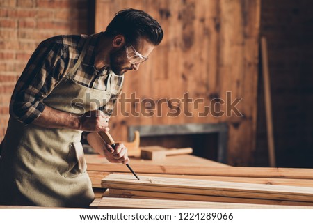 Half turned photo portrait of serious focused concentrated thoughtful handsome bearded strong masculine busy professional foreman builder using equipment wooden plank