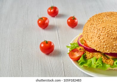 A half of veggie burger with salad, onion rings decorated with fresh cherry tomatoes on the gray concrete background with free copy space. Vegetarian sandwich. Close up view - Powered by Shutterstock