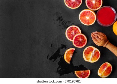 Half-blood oranges cut in pieces over dark rustic background with freshly squeezed juice. Top view