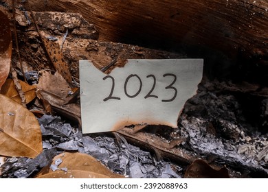 half-burnt notepad with 2023 written on it in the fireplace. new life and new year 2024 concept. 2023 paper is burning, say goodbye to 2023